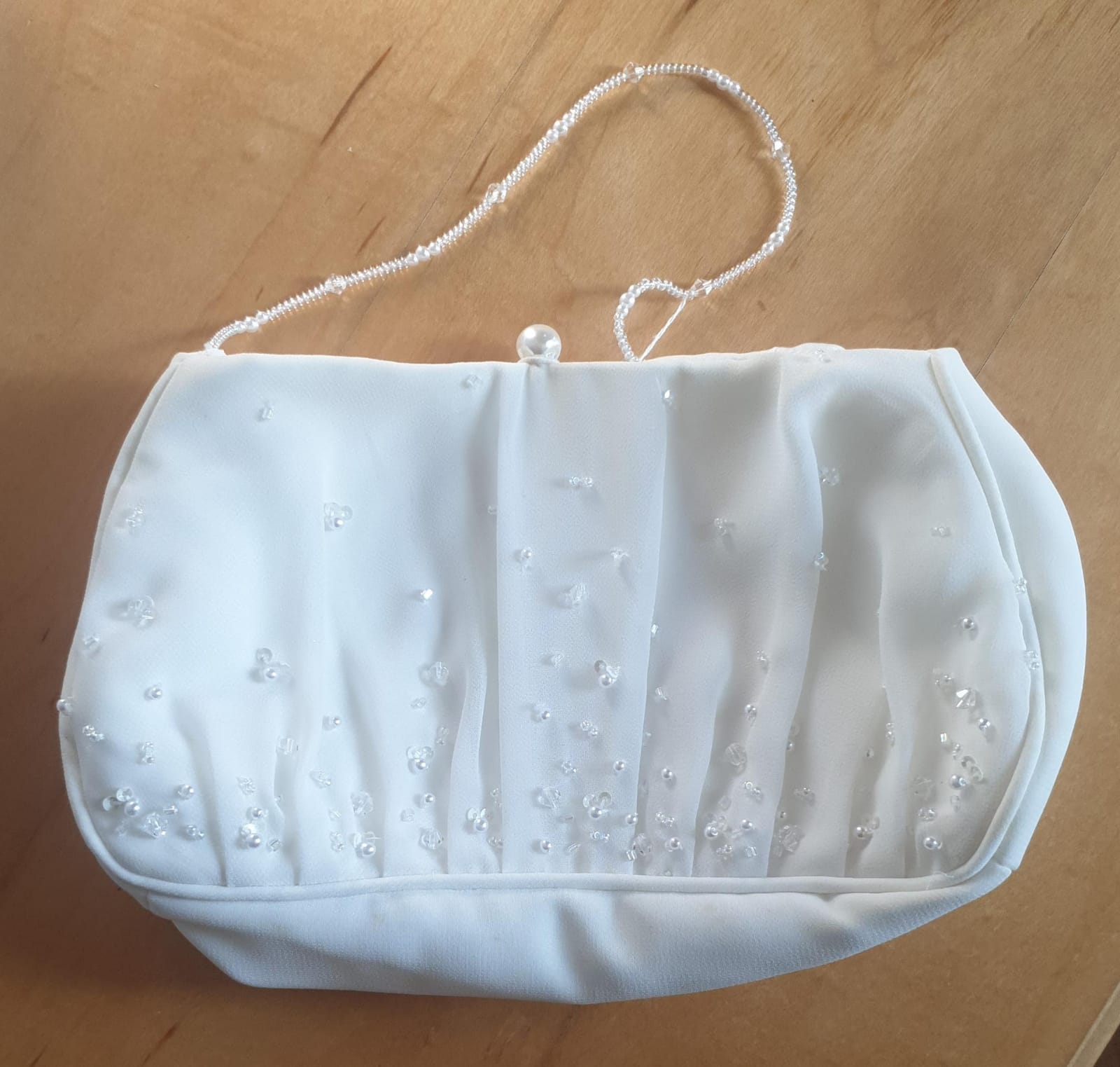 White handbag with pearl embellishments on a wooden surface